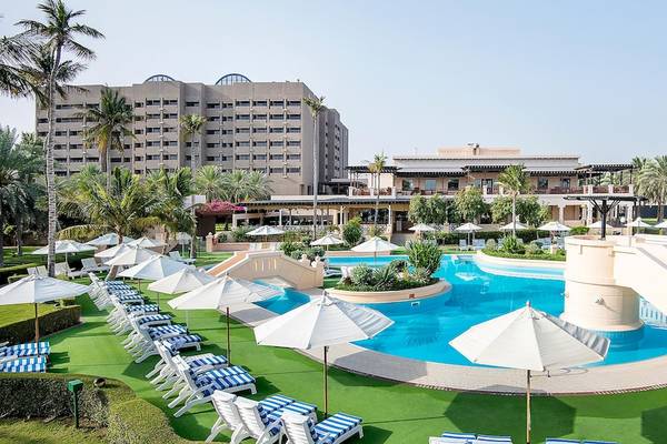 Außenbereich des InterContinental Muscat Hotels mit Swimmingpool, Sonnenliegen und weißen Sonnenschirmen.