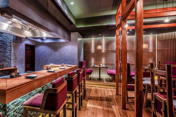 Innenraum des Sushi-Restaurants im InterContinental Muscat mit hölzerner Theke und roten Stühlen.