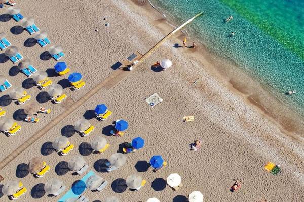 Luftaufnahme des Strandes des Mediterranean Hotel in Rhodos mit Sonnenliegen, Sonnenschirmen und Schwimmern im Wasser.