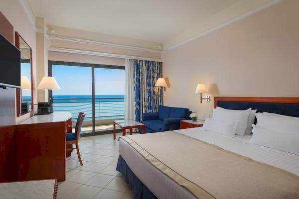 Zimmer im Mediterranean Hotel in Rhodos mit Meerblick, Bett, Sofa und Schreibtisch.