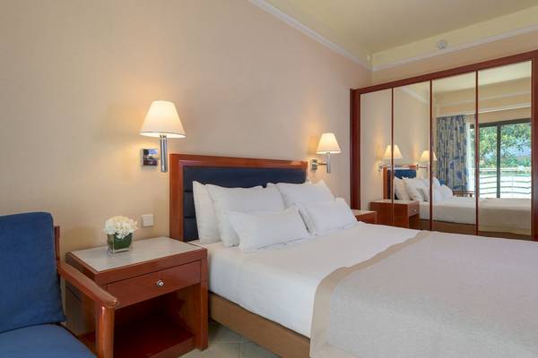Innenansicht eines Schlafzimmers im Mediterranean Hotel auf Rhodos, mit einem Bett, Nachttisch und Spiegelschrank.