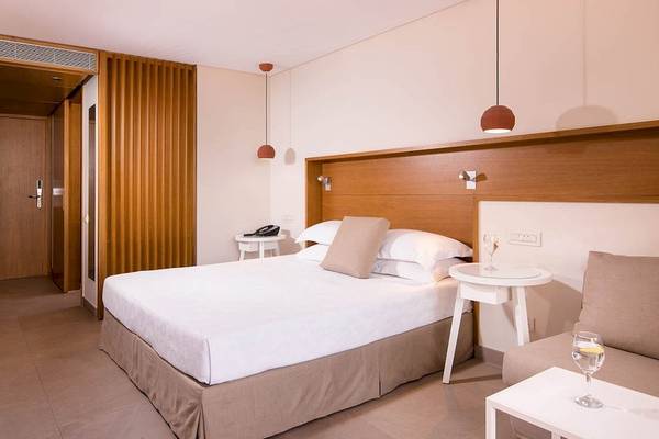 Innenansicht eines Zimmers im Kernos Beach Hotel & Bungalows mit Bett, Nachttischen und offenem Eingang.
