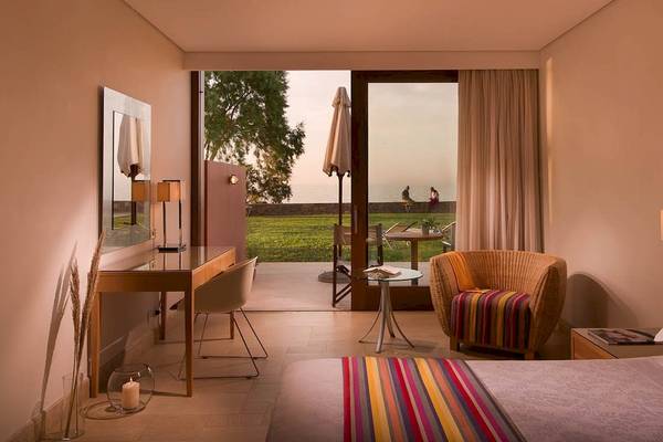 Innenansicht eines Zimmers im Kernos Beach Hotel & Bungalows mit Blick auf eine Terrasse und Meer.