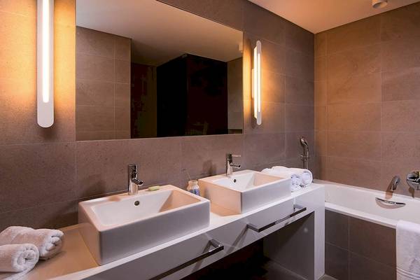 Badezimmer im Kernos Beach Hotel mit zwei Waschbecken, Badewanne und Spiegel.