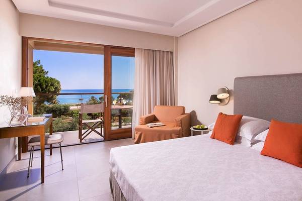 Schlafzimmer im Kernos Beach Hotel mit Meerblick, einem großen Bett, einem Schreibtisch und einem Balkon.