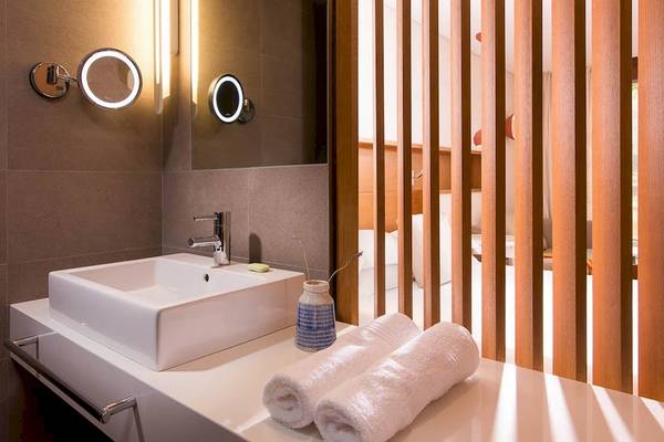 Badezimmer des Kernos Beach Hotel mit Waschbecken, Spiegel und gerollten Handtüchern.