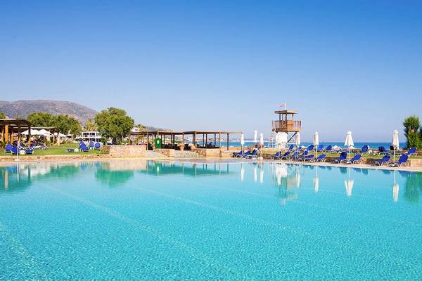 Außenpool des Kernos Beach Hotel mit blauen Liegestühlen und Sonnenschirmen am Strand