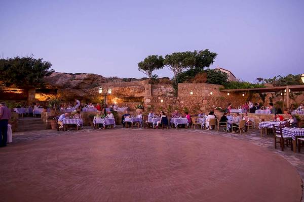 Abendessen im Hotelgarten des Kernos Beach Hotel & Bungalows mit Gästen an blau-weiß karierten Tischen.