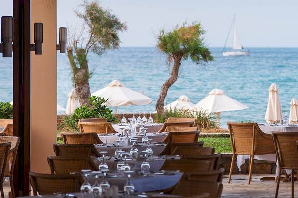 Außenbereich des Kernos Beach Hotel & Bungalows mit Blick auf das Meer und gedeckten Tischen.