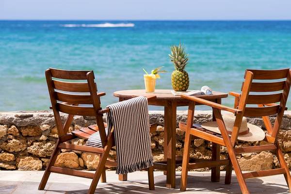 Ein Holztisch mit zwei Stühlen und einer Ananas steht am Strand mit Blick auf das Meer.