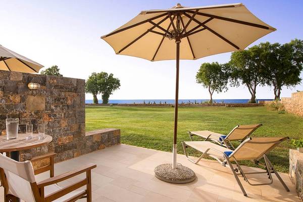 Terrasse mit Strandblick im Kernos Beach Hotel mit Sonnenschirmen, Tisch und Liegestühlen.