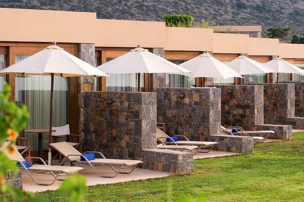 Terrasse mit Liegen im Kernos Beach Hotel & Bungalows mit Steinmauer und Sonnenschirmen.