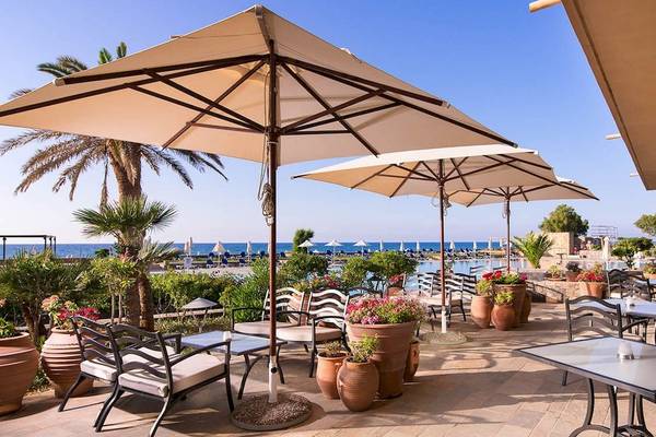 Außenterrasse des Kernos Beach Hotel mit Tischen, Stühlen und Sonnenschirmen am Meer