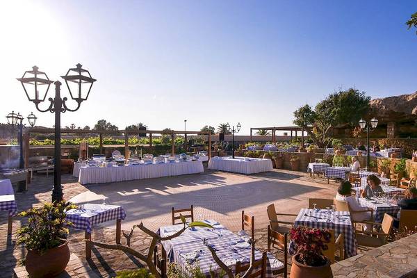 Außenbereich des Kernos Beach Hotel & Bungalows mit blau-weiß karierten Tischen und Stühlen.