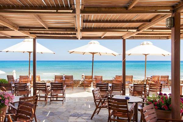 Terrasse des Kernos Beach Hotel mit Blick auf das Meer und holzigen Möbeln