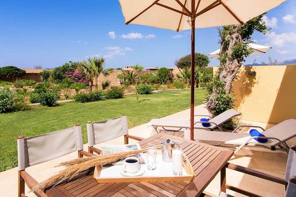 Terrasse des Kernos Beach Hotel mit Liegestühlen, Tisch und Sonnenschirm