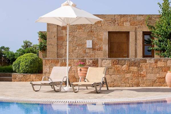 Poolbereich des Kernos Beach Hotel mit Sonnenliegen und einem Schirm.