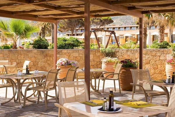Außenbereich des Kernos Beach Hotel & Bungalows mit Tischen und Stühlen unter einem Pergola.