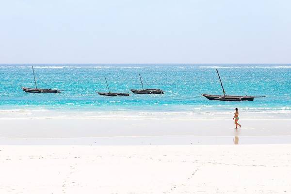 Strand mit Booten im Wasser und einer laufenden Frau