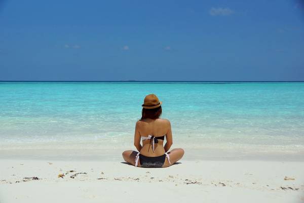 Frau am Strand im Hut sitzend, Blick auf das Meer, Baobab Beach Resort