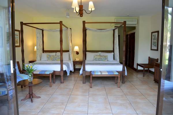 Zwei Doppelbetten im Zimmer im Baobab Beach Resort & Spa mit Blumenvase, Tisch und Holzmöbeln.