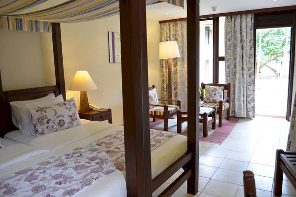 Schlafzimmer mit Baldachin-Bett im Baobab Beach Resort & Spa, inklusive Nachttisch, Lampe und Sessel.