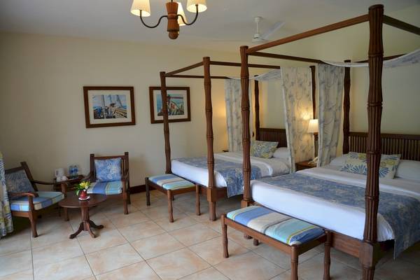 Schlafzimmer im Baobab Beach Resort & Spa mit drei Himmelbetten, zwei Sesseln und einem Tisch.