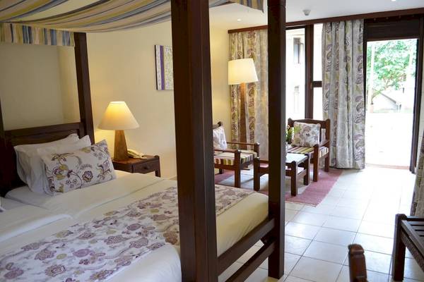 Schlafzimmer im Baobab Beach Resort & Spa mit vierposterbett, nebenstehendem nachttisch und offener tür.