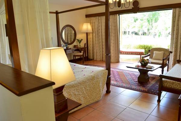 Ein elegant eingerichtetes Zimmer im Baobab Beach Resort & Spa mit einem Himmelbett, einem Schreibtisch, Stühlen und einem großen Fenster mit Ausblick.