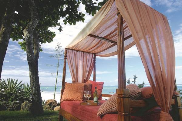 Ein Bett unter einem Baldachin am Strand im Baobab Beach Resort & Spa mit Kissen und Weinglas.