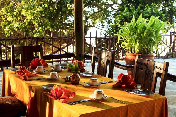 Tisch im Garten des Hotels Baobab Beach Resort & Spa, gedeckt mit roten Servietten, Tassen und Tellern.
