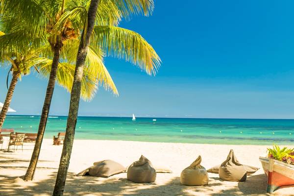 Strand des Maritim Resort & Spa Mauritius mit Palmen, Lounge-Sesseln und einem Boot