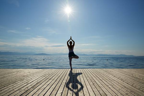 Eine Person praktiziert Yoga in einer Balance-Pose auf einer Holzplattform am Meer.