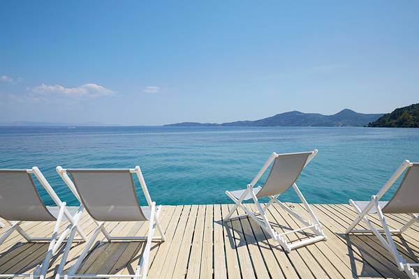Vier weiße Sonnenliegen auf einer Terrasse mit Blick auf das Meer
