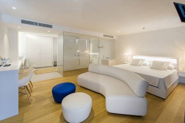 Innenansicht eines Zimmers im Vibra Algarb Hotel mit weißem Bett, Couch, blauem Hocker und weißem Schreibtisch.