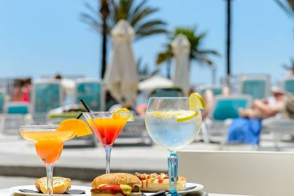 Drei Cocktails und ein Essensteller mit Burger und Hotdog auf einer Terrasse im Hotel.