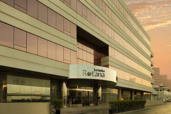 Außenansicht des Jumeira Rotana Hotels bei Sonnenuntergang mit reflektierenden Glasfassaden und Namensschild.