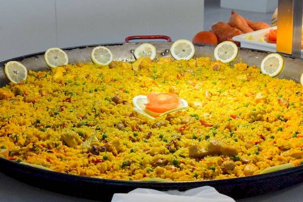 Großer Teller mit Paella, gefüllt mit Reis, Gemüse und Fleisch, dekoriert mit Zitronenscheiben.
