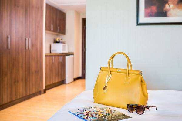 Gelbe Lederhandtasche auf einem Bett mit einer Brille und einer Zeitschrift