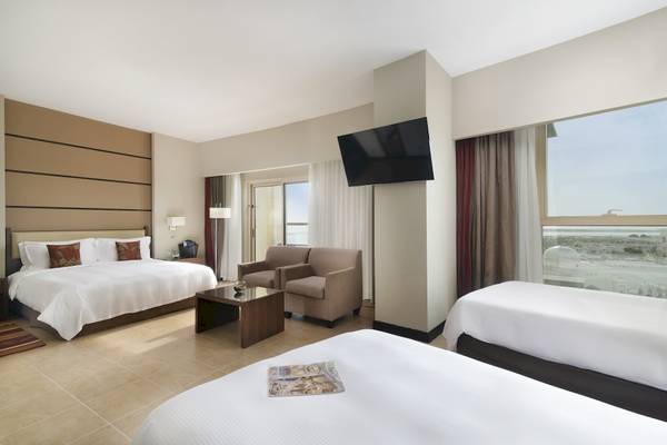 Dreibettzimmer im Khalidiya Palace Rayhaan mit zwei Betten, einem Tisch, einem Fernseher und einer Aussicht.