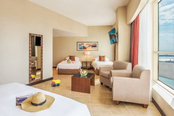 Zimmer im Khalidiya Palace Rayhaan by Rotana Hotel mit zwei Betten, einem Sofa und einem Fenster mit Meerblick.