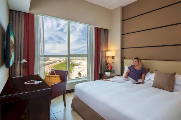 Frau sitzt auf einem Bett im Hotelzimmer des Khalidiya Palace Rayhaan by Rotana und schaut aus dem Fenster.