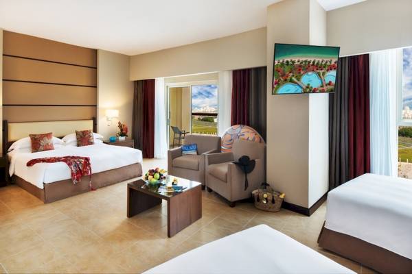 Suite-Innenansicht im Khalidiya Palace Rayhaan by Rotana mit zwei Betten, Wohnzimmerbereich und Fernseher.