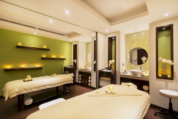 Spa-Behandlungsraum im Khalidiya Palace Rayhaan by Rotana mit zwei Massagetischen, grünen Wänden und Beleuchtung.