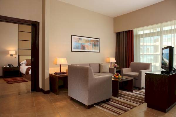 Suite-Wohnzimmer im Khalidiya Palace Rayhaan by Rotana mit Sofa, Tisch, Fernseher und Schlafzimmerbereich.