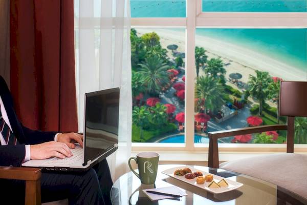 Mann im Hotelzimmer mit Laptop vor Meerblick im Khalidiya Palace Rayhaan by Rotana