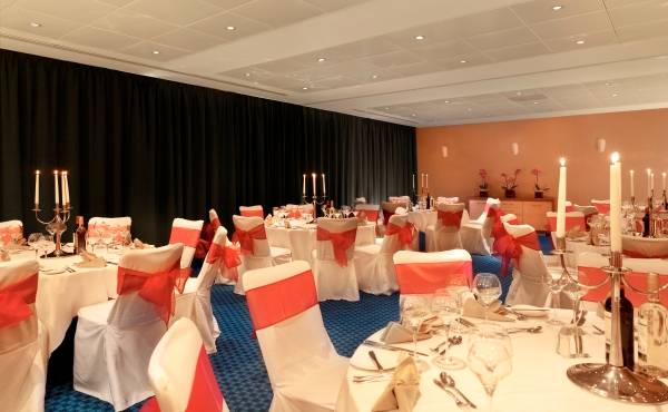 Bankettsaal im Park Plaza County Hall London mit gedeckten Tischen, Kerzen und roten Schleifen.