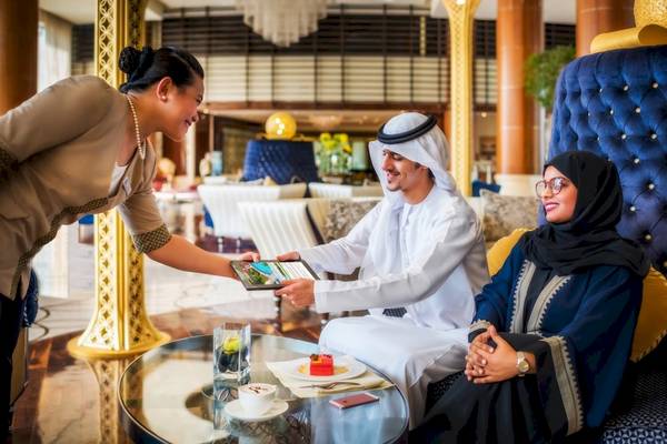 Ein Mitarbeiter im Khalidiya Palace Rayhaan by Rotana Hotel zeigt einem Paar ein Tablet.