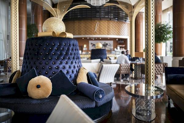 Loungebereich im Khalidiya Palace Rayhaan by Rotana mit blauen und goldenen Kissen, einem runden Tisch und goldenen Wanddekorationen.