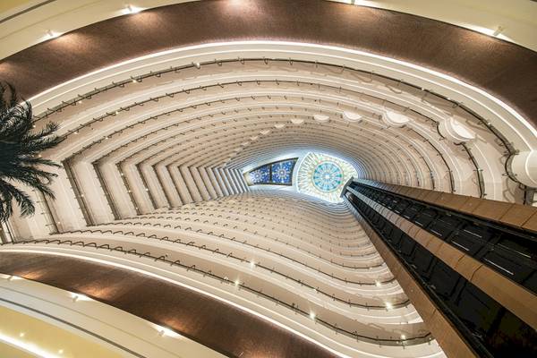 Innenansicht der Lobby des Khalidiya Palace Rayhaan by Rotana mit Blick auf das Atrium und den zentralen Aufzugschacht.